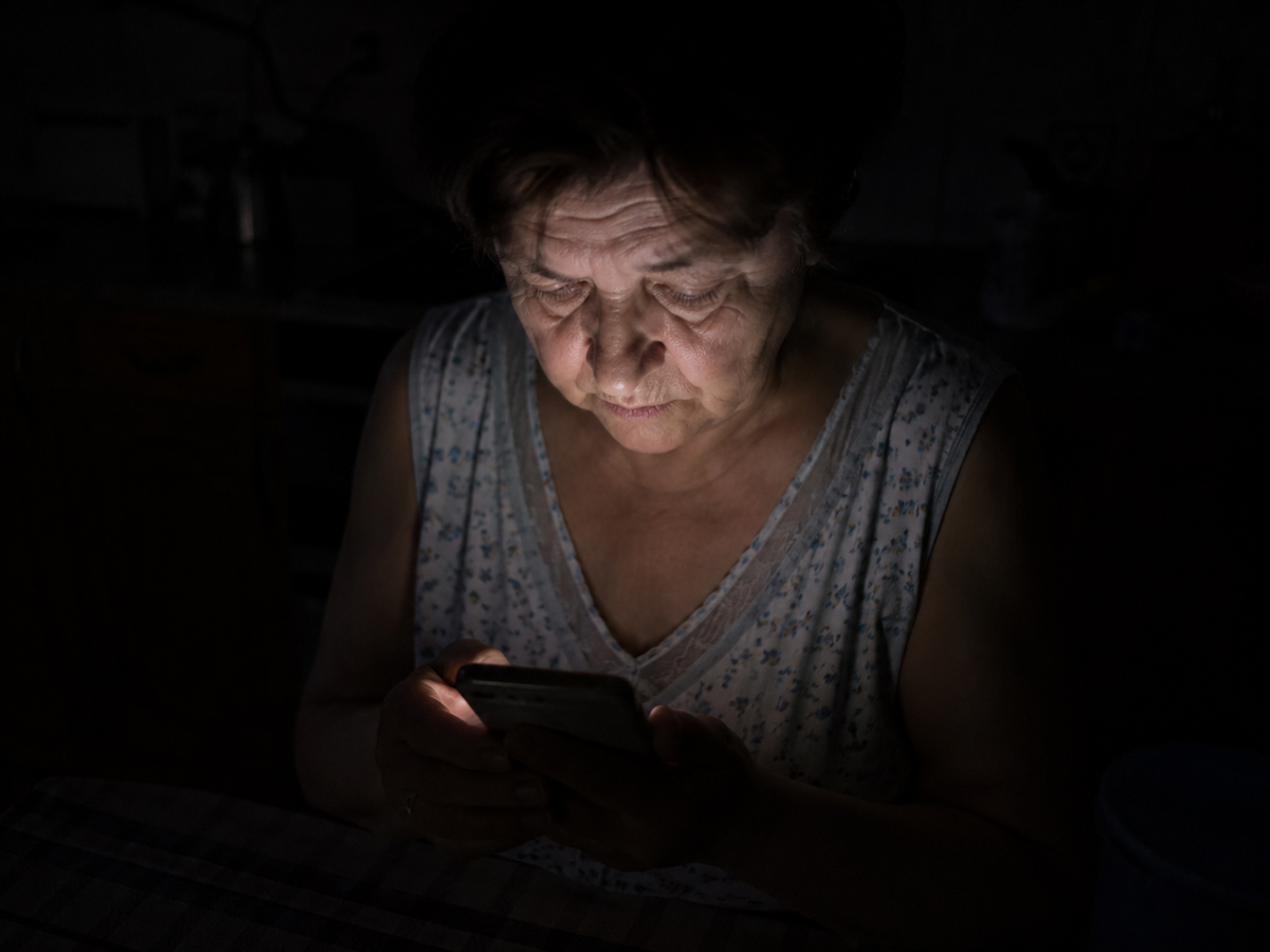 Kobieta w ciemnej kuchni, ekran telefonu oswietla twarz, noc