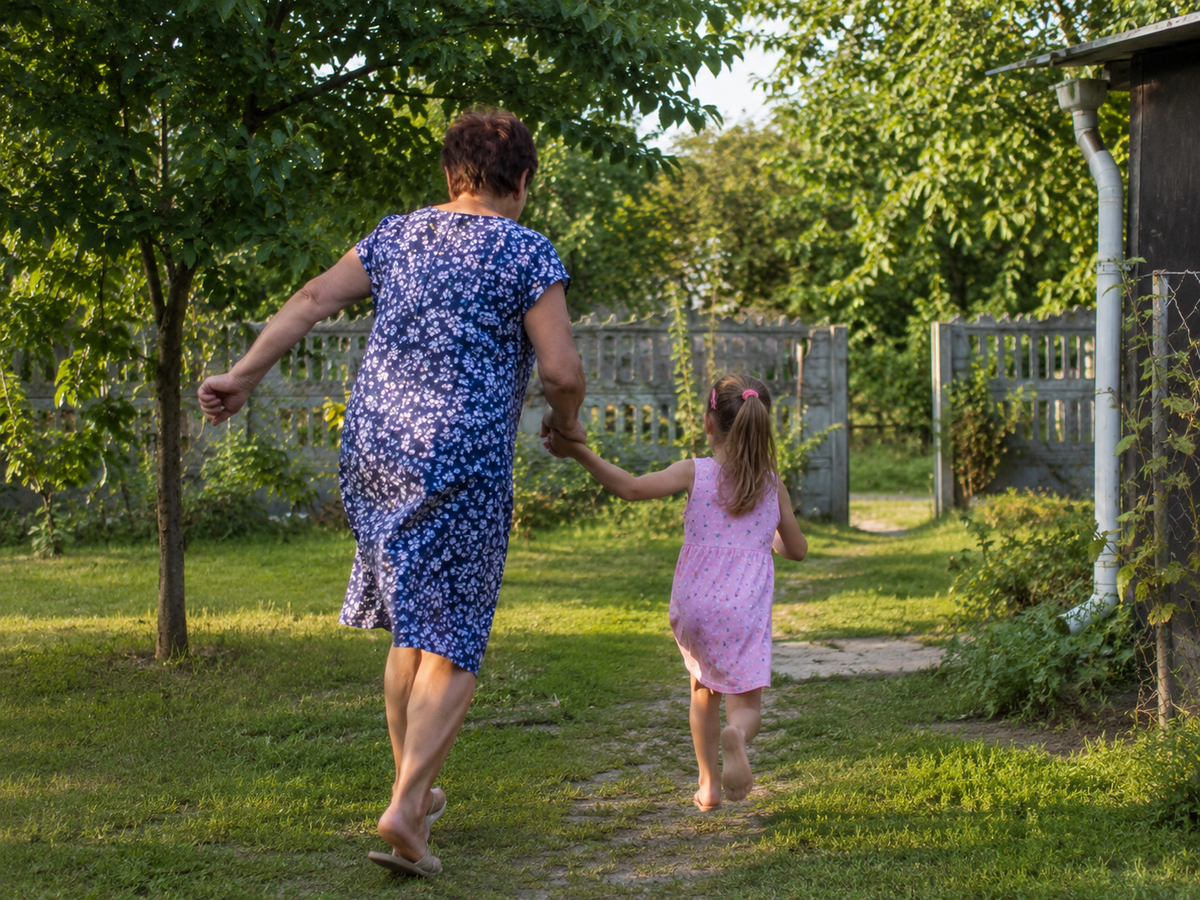 Starsza kobieta i mala dziewczynka biega razem po ogrodzie, sloneczny dzien, radosc